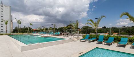 Uma área de piscina com duas piscinas, espreguiçadeiras e palmeiras.