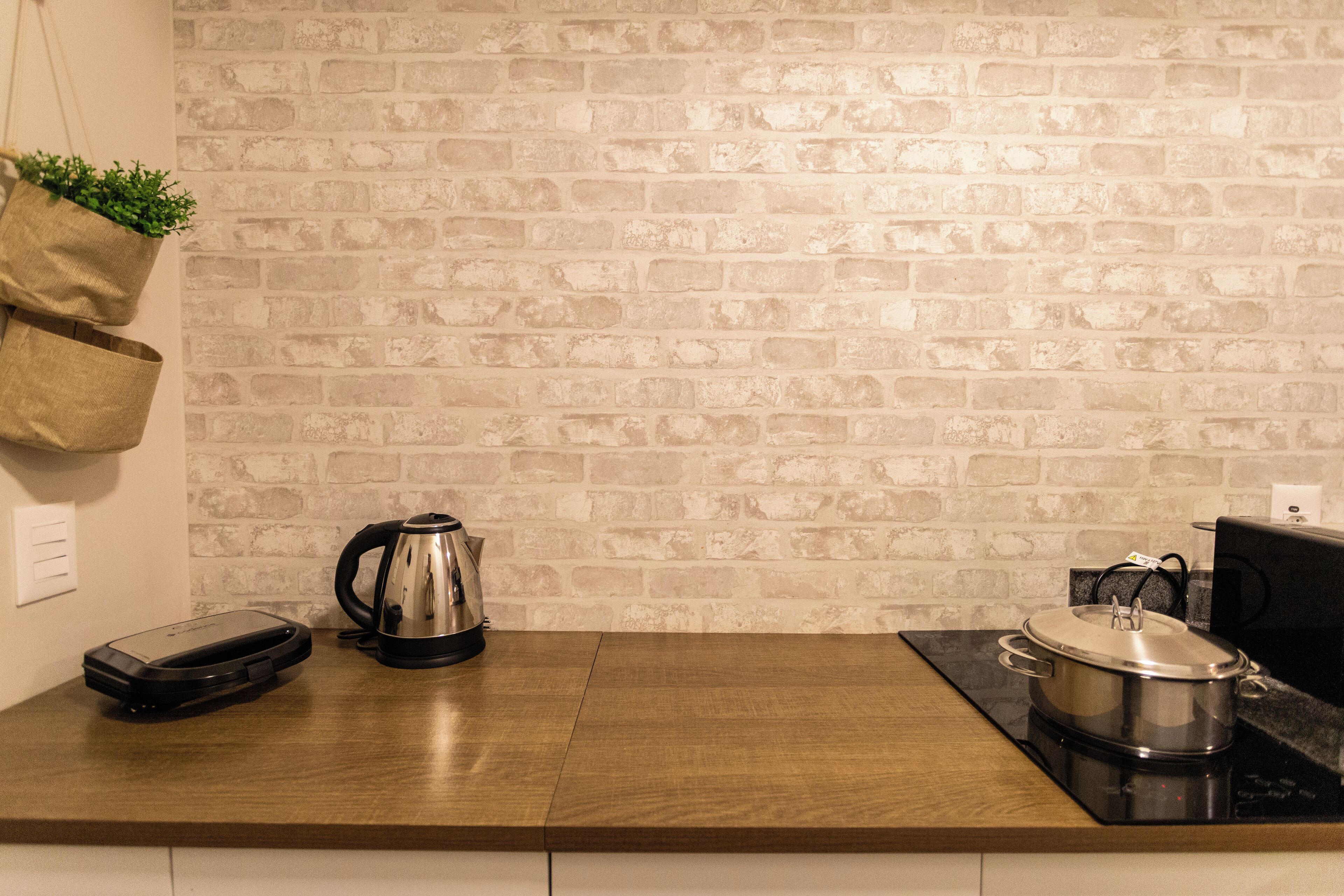 A kitchen with a brick wall, a wooden countertop, a kettle, a pot, and a toaster.