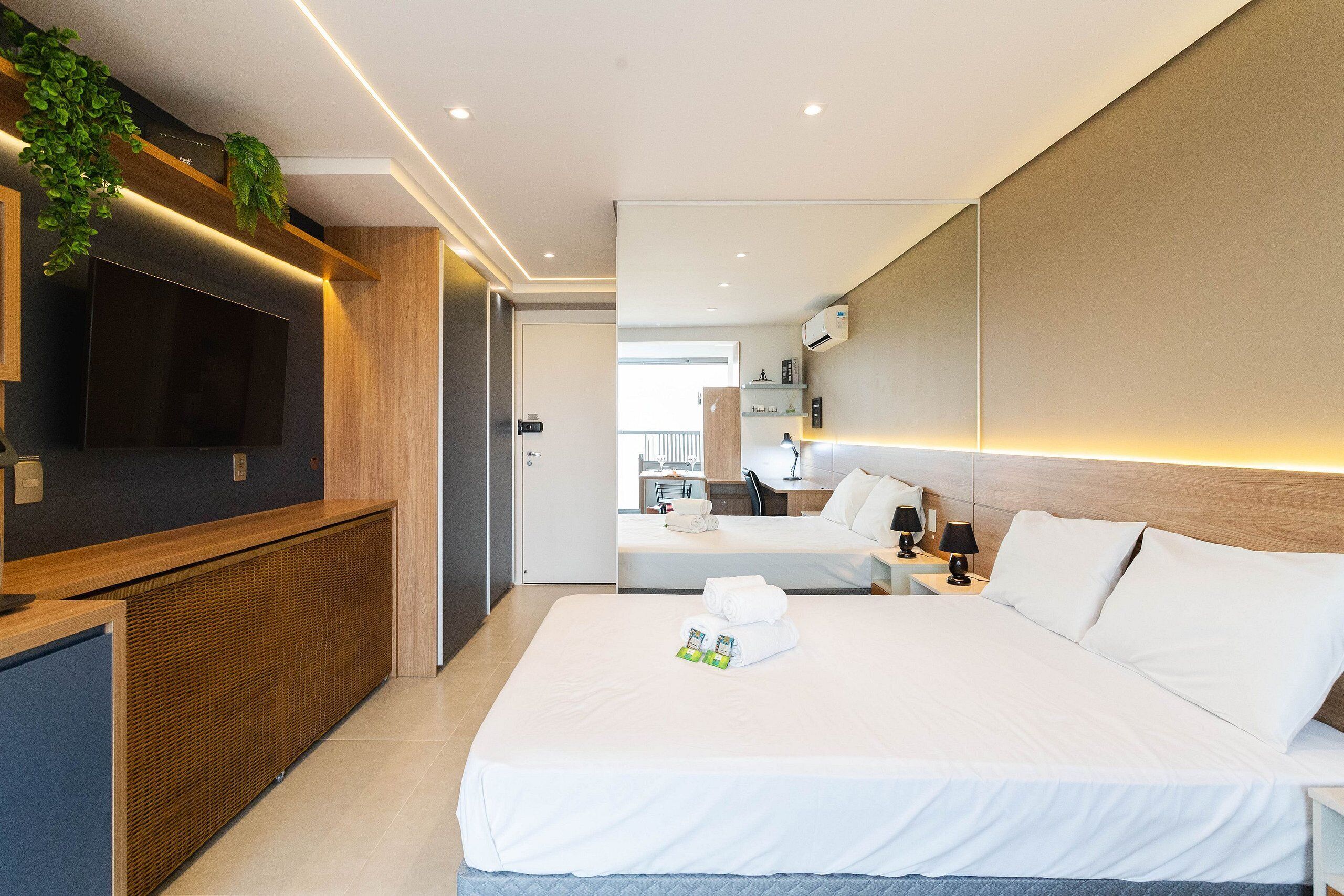 Ein modernes Hotelzimmer mit einem großen Bett, einem Fernseher, einem Schreibtisch und einem Badezimmer im Hintergrund.