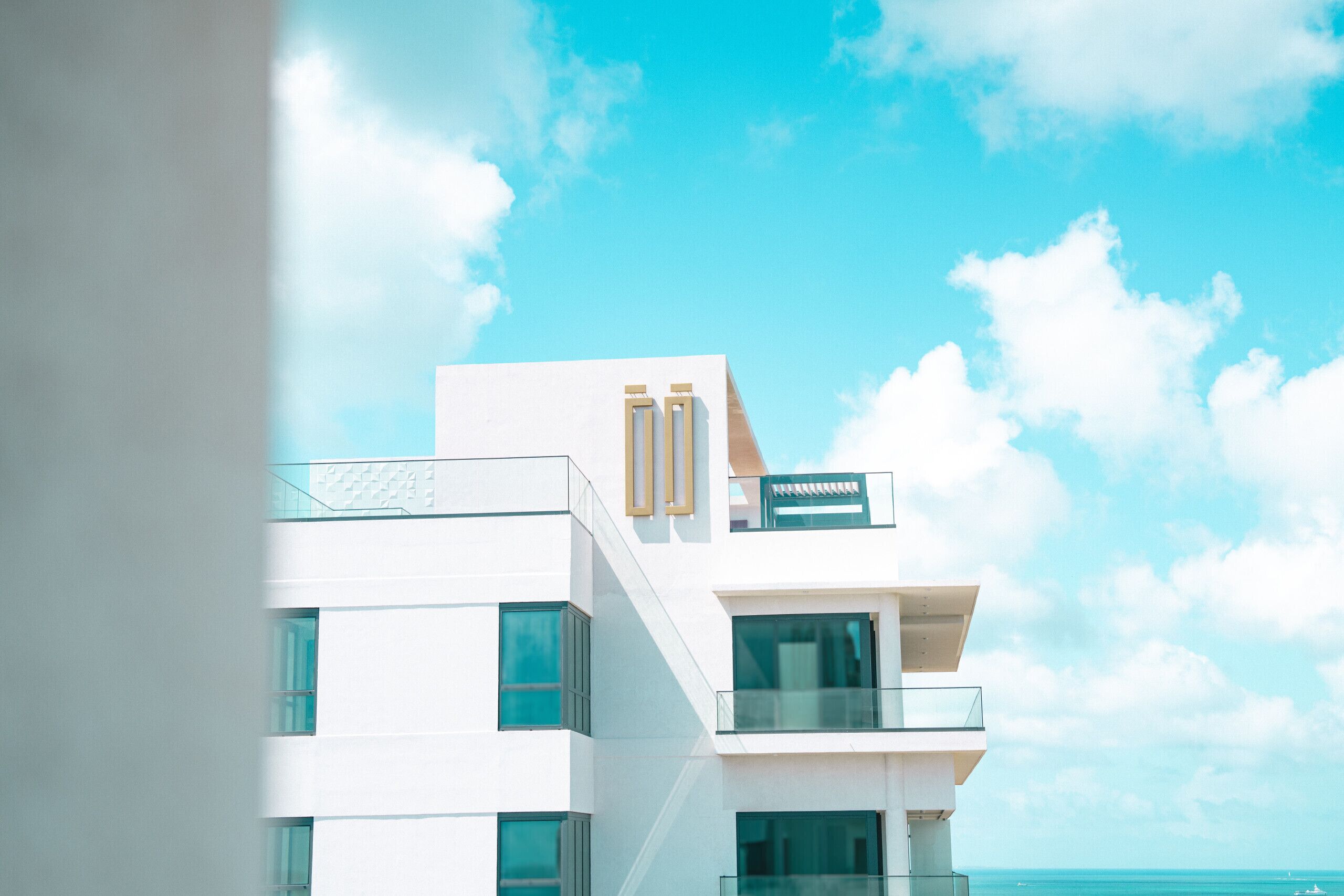 A modern hotel with a white facade, multiple balconies, and a clear view of the ocean.