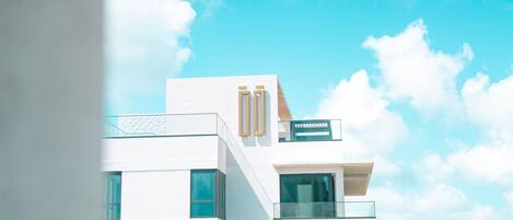 A modern hotel with a white facade, multiple balconies, and a clear view of the ocean.