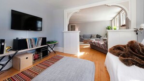 Un dormitorio moderno con un televisor de pantalla plana, una estantería, una cama con una manta de piel sintética y vistas al área de estar.