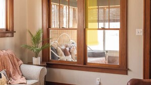 Une pièce chaleureuse avec une grande fenêtre, une plante en pot et un fauteuil recouvert d’une couverture.