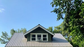 Une maison à deux étages, avec un toit en métal, un porche à l’avant et un chemin menant à la porte.