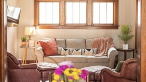 Un salon confortable avec un canapé, deux fauteuils, une table basse et un téléviseur fixé au mur.
