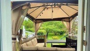 Un espace extérieur abrité, aménagé avec un banc rembourré et une table, donnant sur un jardin.