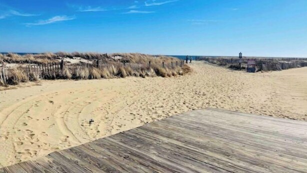 Une plage de sable avec une promenade en bois et un système de dunes.