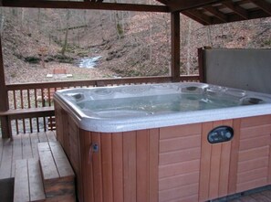 A hot tub with a wooden deck and a view of a forested area. - 3BR, 2 Bath Cabin with full kitchen, living room, hot tub and spacious backyard. (Putney)