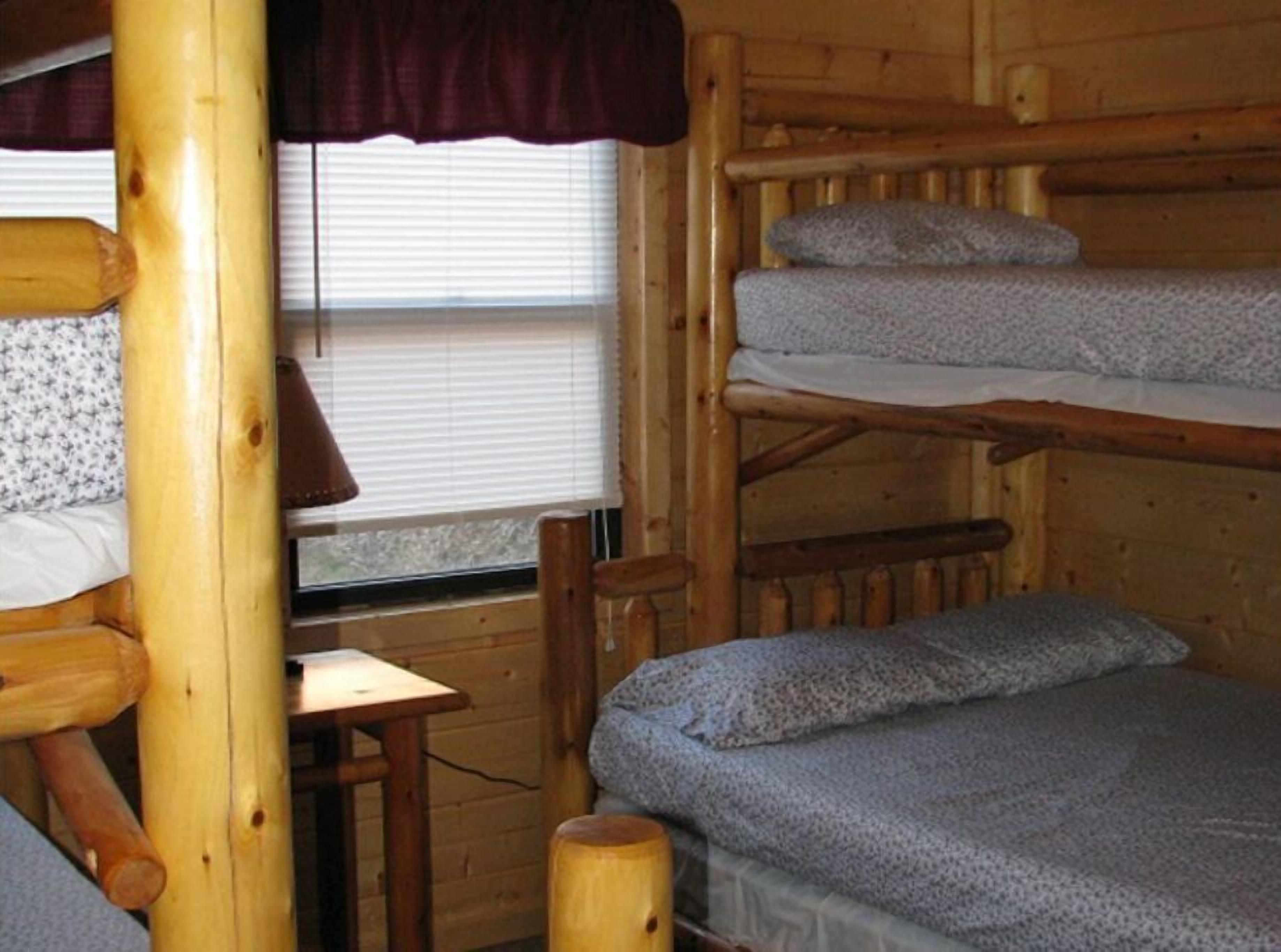 Una cabaña con literas, una mesita de madera y una ventana con persianas.