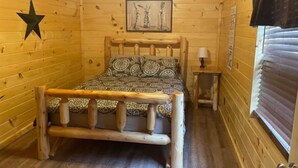 A wooden cabin room with a bed, a star decoration, a framed picture, a nightstand, and a window with blinds. - 3BR, 2 Bath Cabin with full kitchen, living room, and hot tub. (Putney)