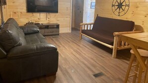 A cozy living room with a leather sofa, a wooden table, and a TV mounted on the wall. - 3BR, 2 Bath Cabin with full kitchen, living room, and hot tub. (Putney)
