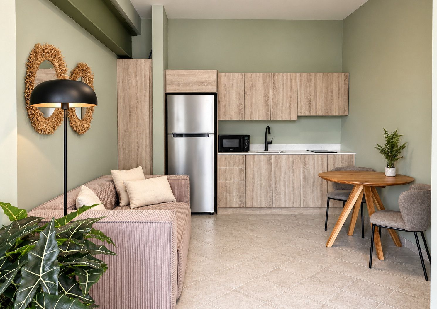 Un espacio habitable compacto con kitchenette, un sofá, una mesa de comedor y una planta en maceta.