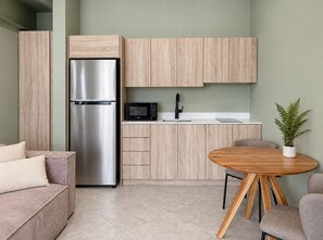 Cocina compacta con refrigerador integrado, microondas y lavamanos, una mesa de madera redonda y una planta en maceta.