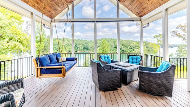 A covered outdoor deck with a swing seat, wicker furniture, and a view of the surrounding landscape.