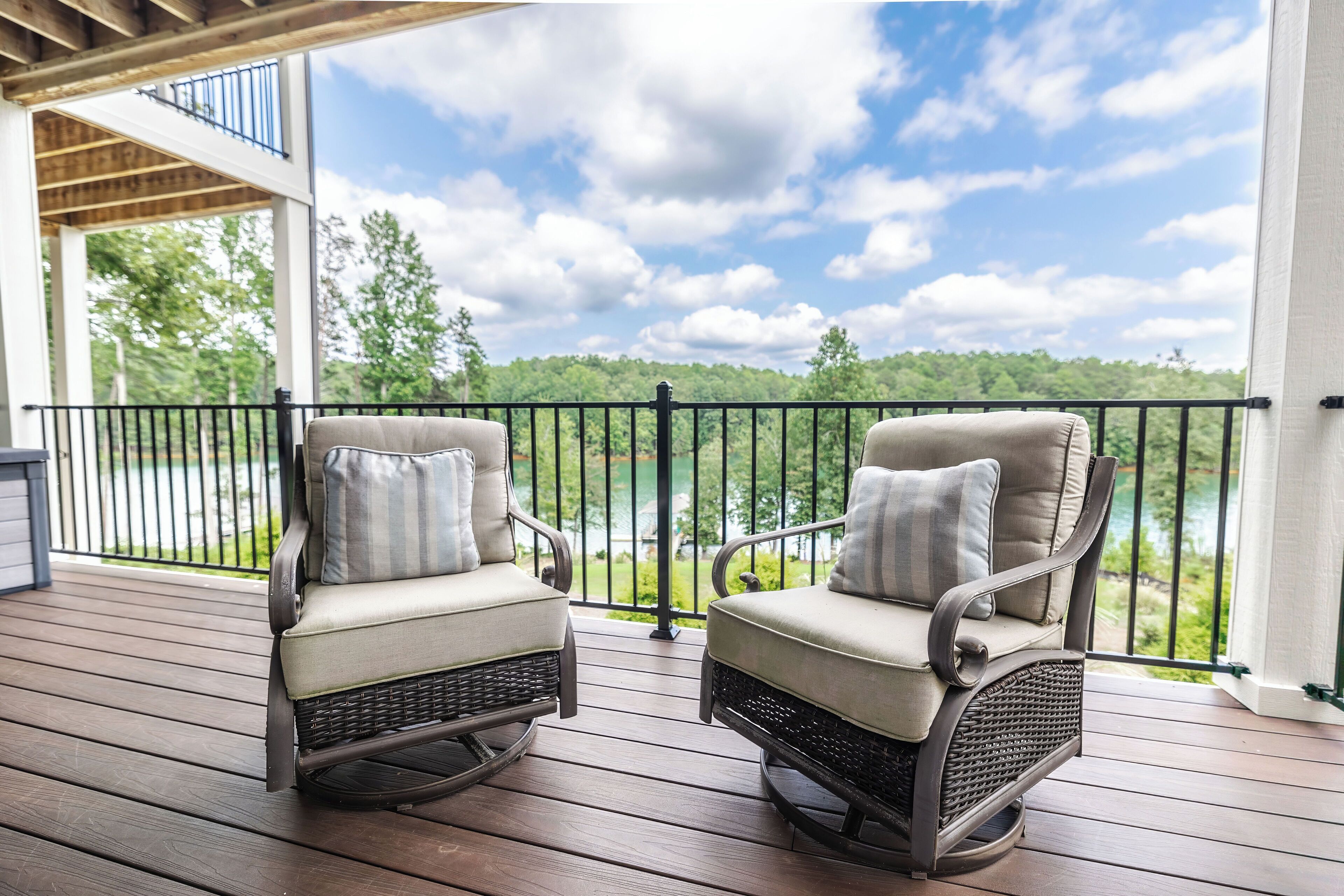 Two rocking chairs on a wooden deck with a view of a lake and trees.
