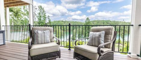 Two rocking chairs on a wooden deck with a view of a lake and trees.