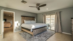 A bedroom with a large bed, a ceiling fan, a view through a sliding glass door, and a small side table. - Beautiful views with a heated pool and plenty of room for large families! (Fountain Hills)
