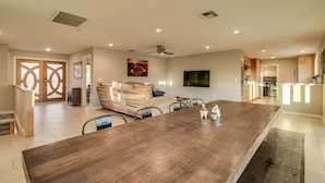 A spacious living area with a large wooden dining table, a sofa, and a flat-screen TV mounted on the wall. - Beautiful views with a heated pool and plenty of room for large families! (Fountain Hills)