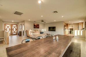 A spacious living area with a large wooden dining table, a sofa, and a flat-screen TV mounted on the wall. - Beautiful views with a heated pool and plenty of room for large families! (Fountain Hills)