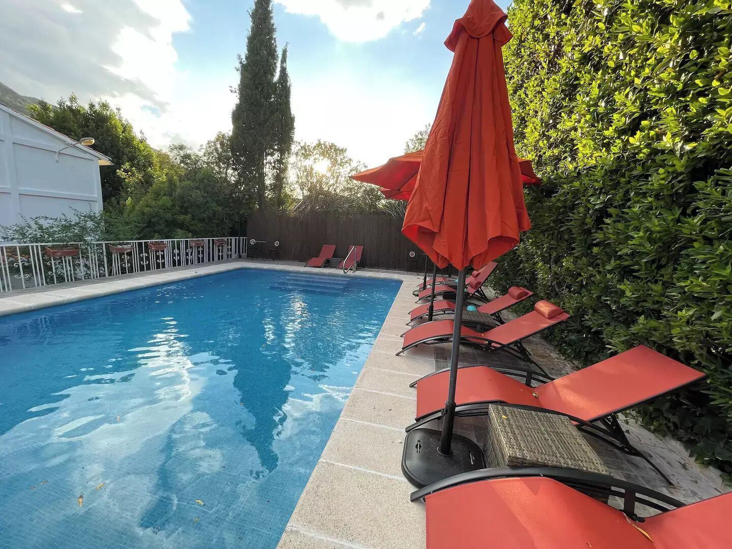 Une piscine à l’eau d’un bleu cristallin, entourée de chaises longues rouges et d’un parasol orange.
