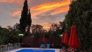 A swimming pool with red lounge chairs and umbrellas, surrounded by greenery and a wooden fence. - Villa GAN EDEN a gem in a privileged environment (Barx)