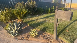 A mailbox in a yard with a fence, a house, and a railroad crossing in the background. - Town House Motel (Sanger)