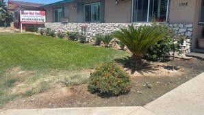 A building with a stone facade, a green lawn, and a flower bed with marigolds. - Town House Motel (Sanger)