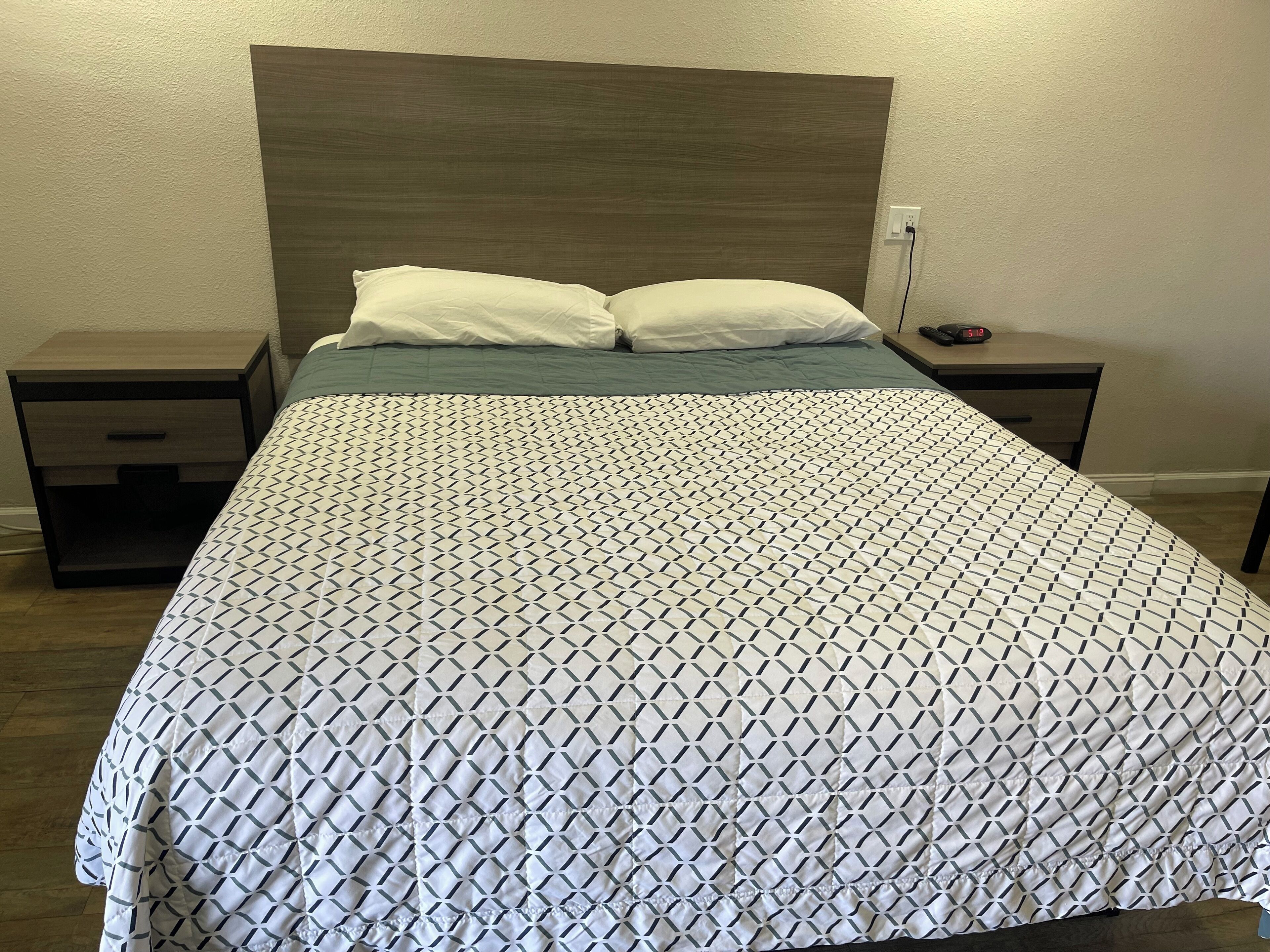 Ein ordentlich bezogenes Bett mit einem geometrisch gemusterten Bettbezug, zwei weiße Kissen und ein Holz-Kopfstück.