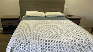 Una cama bien hecha con un edredón estampado con motivos geométricos, dos almohadas blancas y un cabecero de madera.