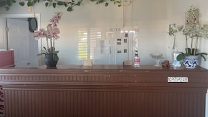 A reception desk with a 'NO PETS PLEASE' sign, potted orchids, a ceiling fan, and a 'CHECK OUT TIME 1AM' sign. - Town House Motel (Sanger)