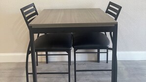 A dining area with a rectangular table and four chairs, a flat-screen TV mounted on the wall above, and a light-colored textured wall. - Town House Motel (Sanger)