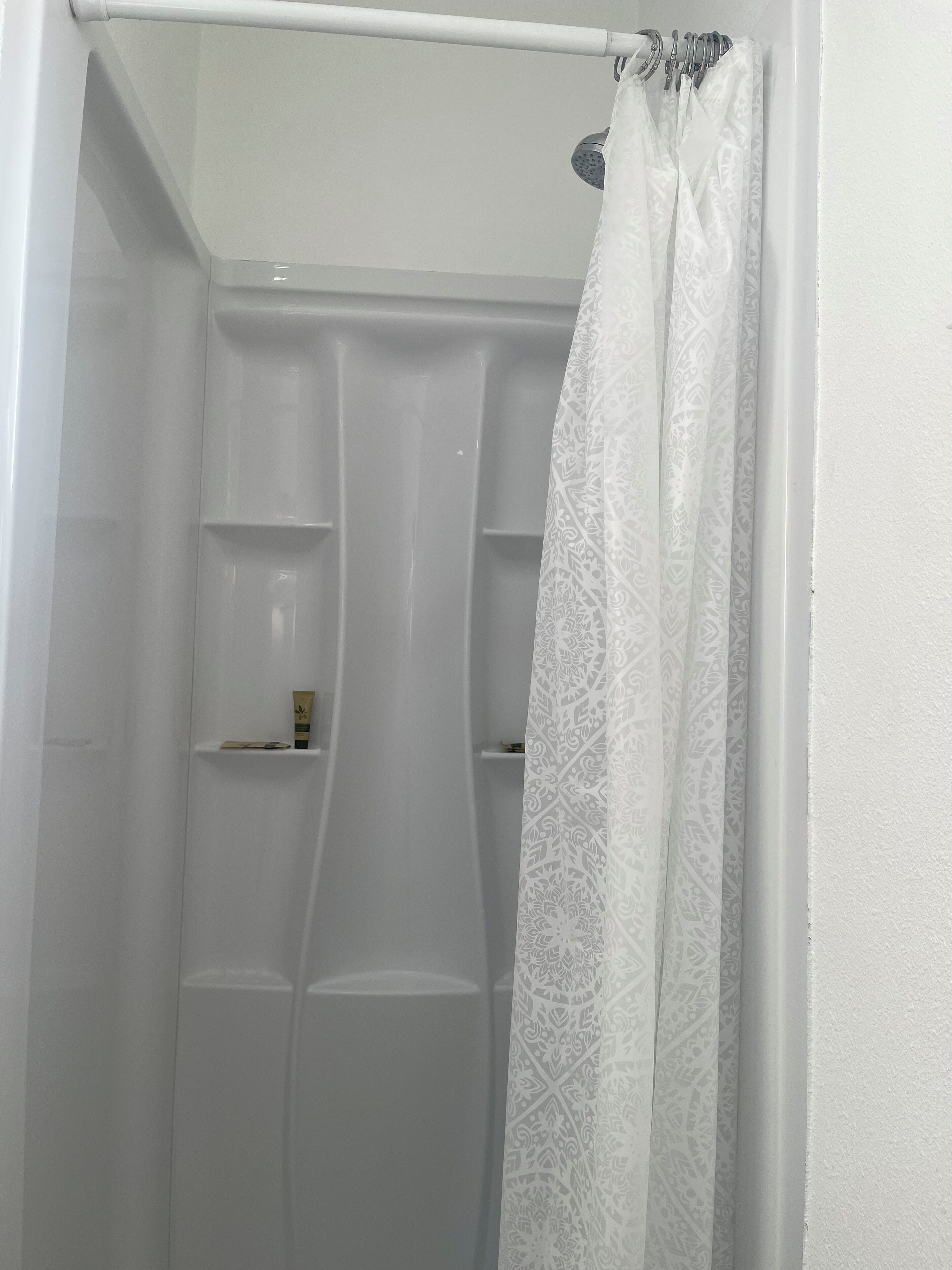 A shower area with a white shower curtain and a handheld showerhead.
