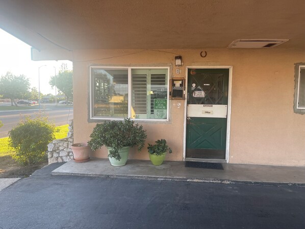 A building entrance with a green door labeled "Office," a window with blinds, and potted plants. - Town House Motel (Sanger)