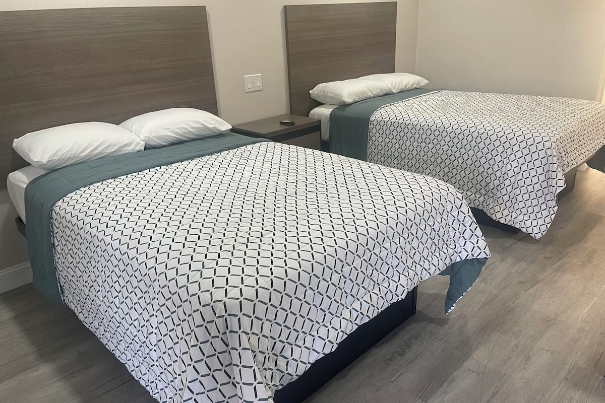 A hotel room with two beds, each with a geometric-patterned bedspread and white pillows.
