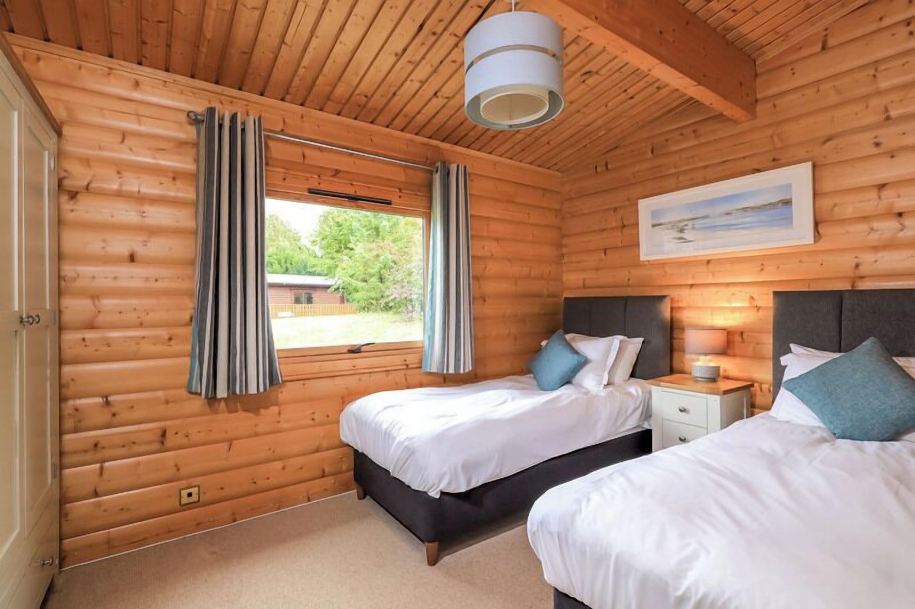 Une chambre rustique en bois avec deux lits, une table de chevet, une fenêtre avec des rideaux et un tableau au mur.