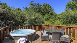 A hot tub on a wooden deck with wicker furniture and a wooden railing. - 3 Bedroom, 5 star, award winning Lodge with luxurious hot tub (sleeps 6) (Winchester)