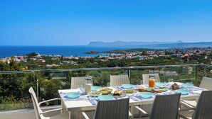 Una mesa lista para una comida, con vistas panorámicas a un pueblo costero y montañas al fondo.