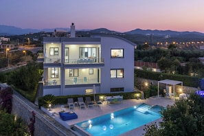 Una casa moderna de dos pisos con piscina, mobiliario exterior y vistas del paisaje circundante.