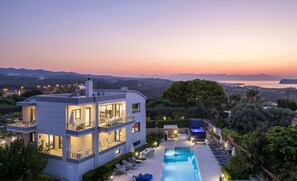 Un edificio moderno de dos pisos con piscina en la azotea, rodeado de exuberante vegetación y vistas a un paisaje pintoresco.