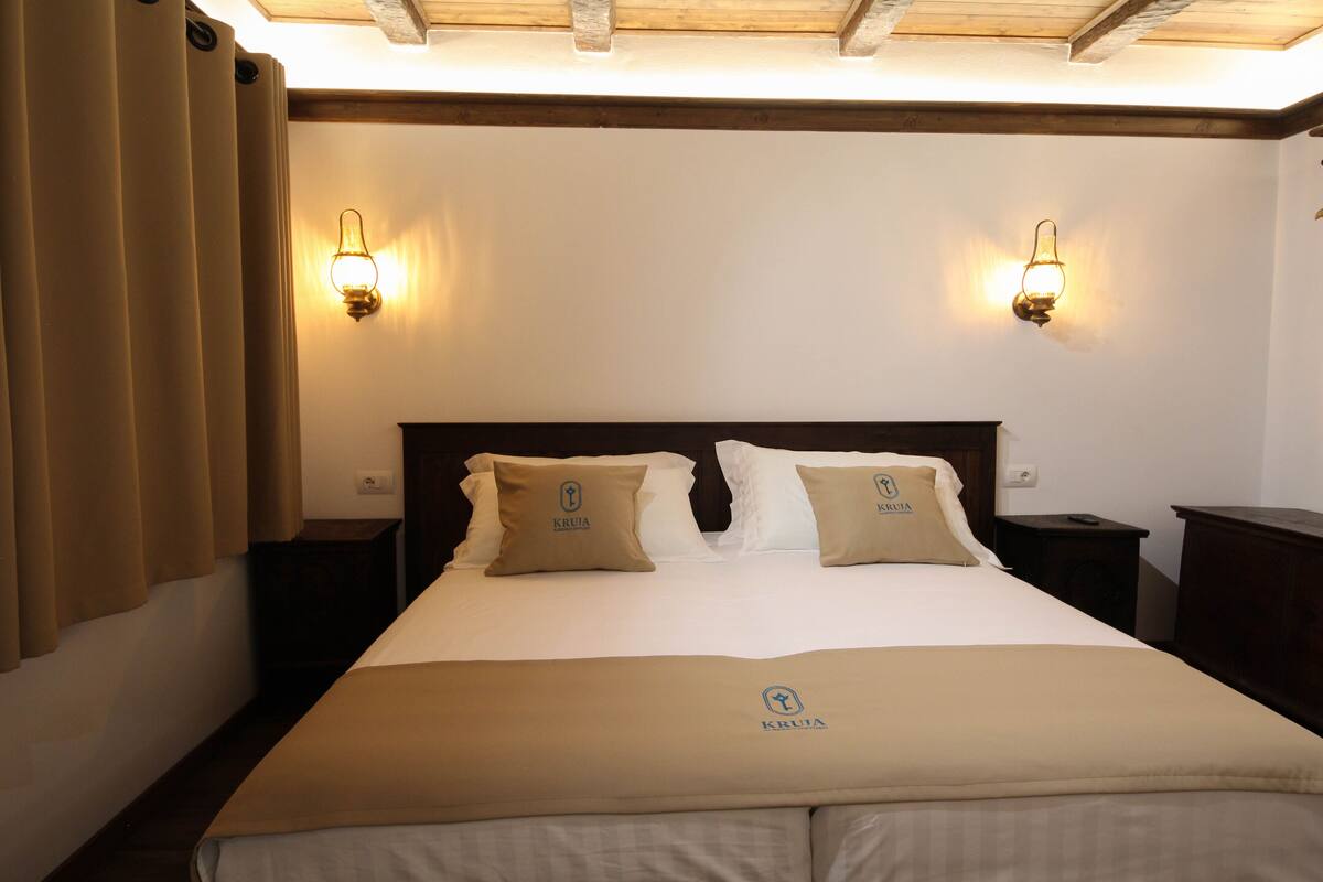 A hotel room with a large bed, two bedside tables, a headboard, and two wall-mounted light fixtures.