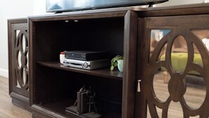 Um centro de entretenimento de madeira com uma televisão de tela plana em cima, um leitor de DVD e um console de jogos na prateleira inferior.