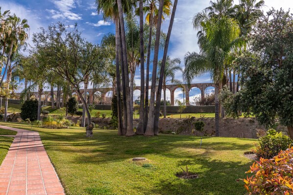 A garden with palm trees, a brick pathway, and an arched bridge in the background.