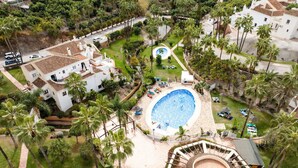 Vue aérienne d’un complexe hôtelier doté d’une piscine centrale, de plusieurs villas et d’un aménagement paysager luxuriant.