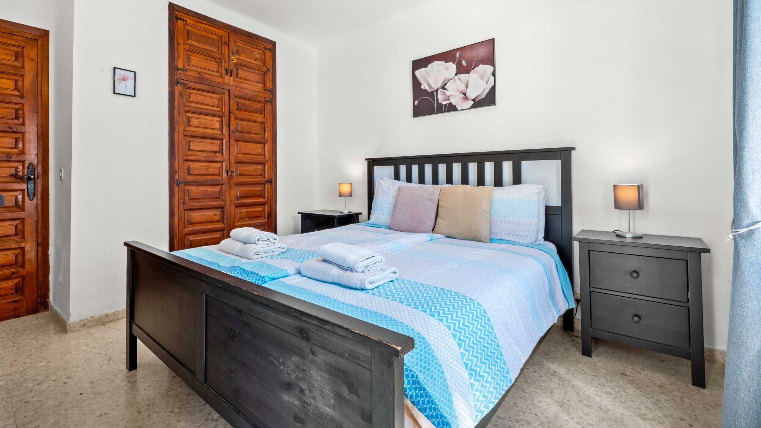 Um quarto com uma cama, duas mesas de cabeceira, um guarda-roupa de madeira e um quadro na parede.