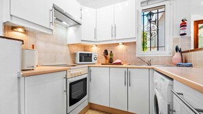 Eine moderne Küche mit weißen Schränken, einer Mikrowelle, einem Backofen, einer Spüle und einem Fenster mit dekorativem Eisengitter.