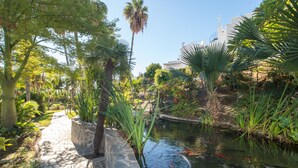 Un jardin avec un sentier en pierre, un bassin avec des carpes koï et diverses plantes tropicales.