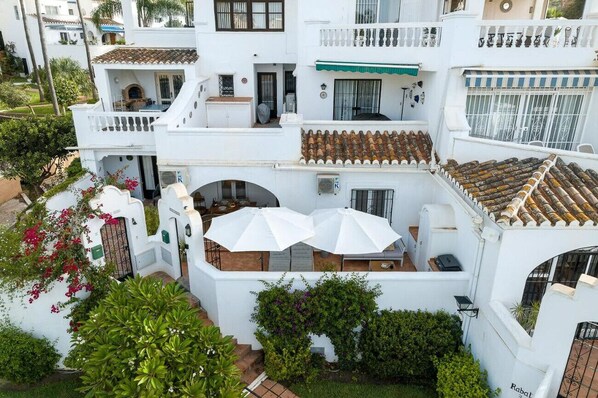 A white building with a tiled roof, a balcony with white umbrellas, and a small garden area. - Rabat 2 - El Oasis de Capistrano! (Nerja)