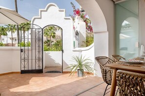 A patio with a dining table and chairs, a decorative gate, and a view of palm trees and a building. - Rabat 2 - El Oasis de Capistrano! (Nerja)