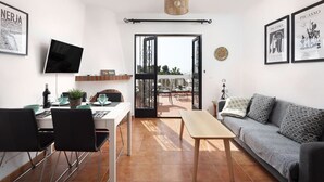 Un salon moderne avec un canapé, une table à manger et des chaises. Un téléviseur est fixé au mur, et des œuvres d’art sont exposées sur les murs.