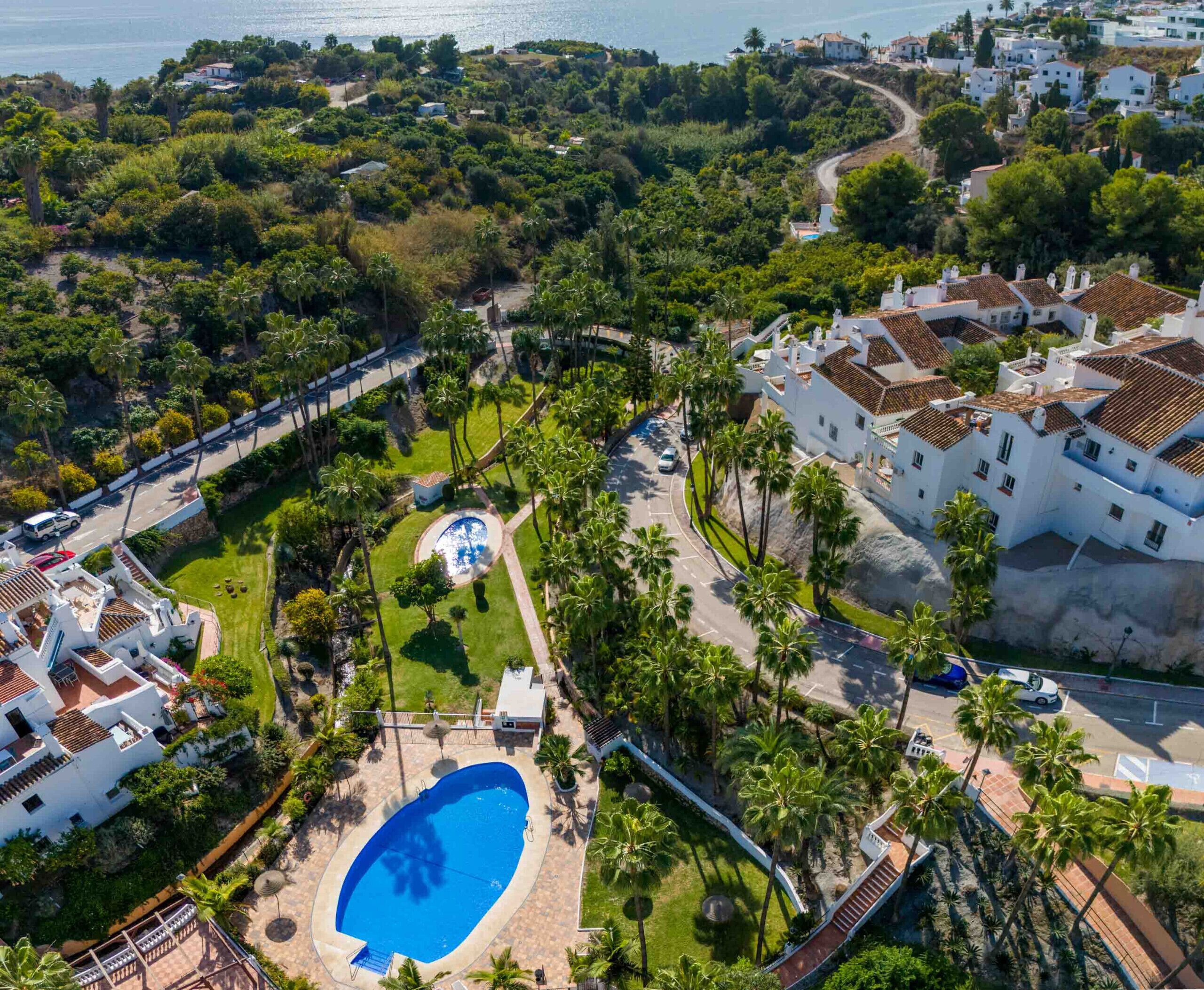 Luftaufnahme eines Resorts mit Schwimmbad, Palmen und weißen Gebäuden mit roten Ziegeldächern.